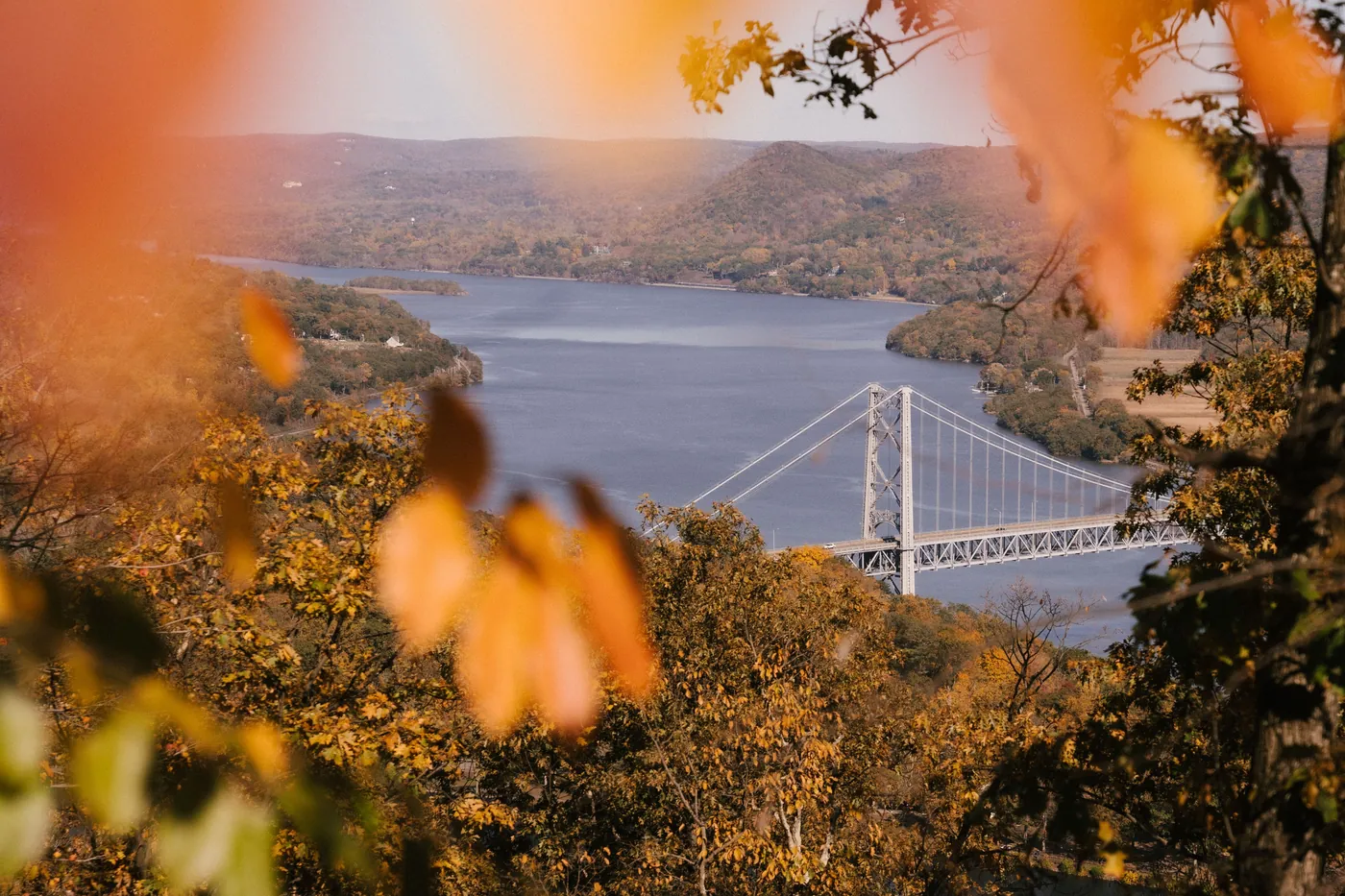 Aerial-perspective view of the Hudson Valley with the Bear Mountain Bridge spanning the river, framed by orange and yellow autumn foliage