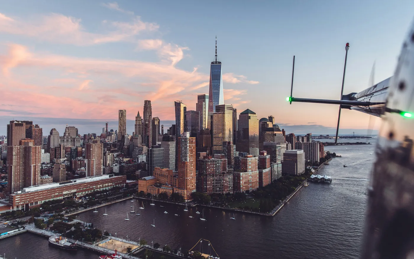 Manhattan-Skyline mit One World Trade Center aus einem Helikopter bei Sonnenuntergang, am Bildrand ist die Kufe des Helikopters zu sehen